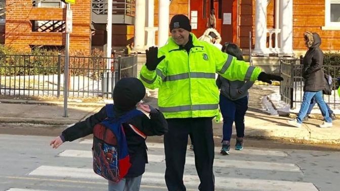 A Waterbury police officer assisting a child across a crosswalk near a school